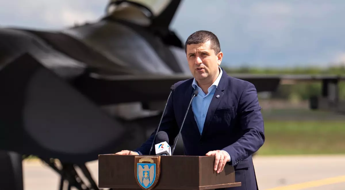 Ministrul Apărării Radu Miruță, în timpul unei conferințe de presă susținută la baza NATO din Lituania, în spatele lui se află un avion de luptă