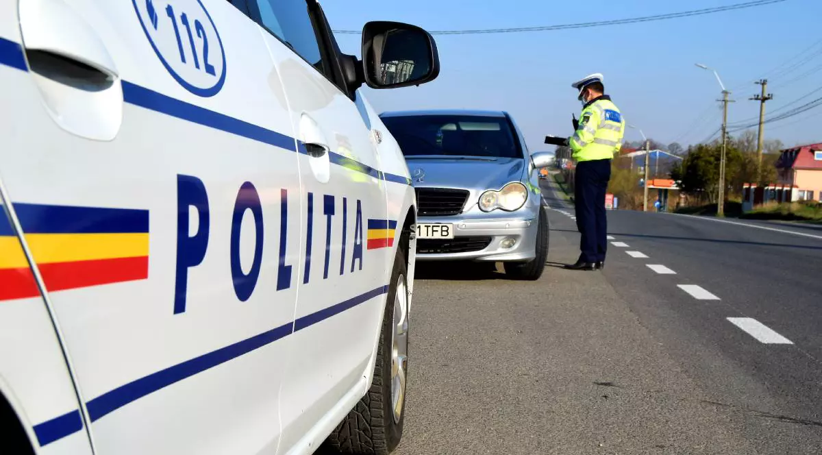 Imagine cu un politist langa un autoturism, noteaza un proces verbal, in prim plan masina politiei, pe un drum din Romania