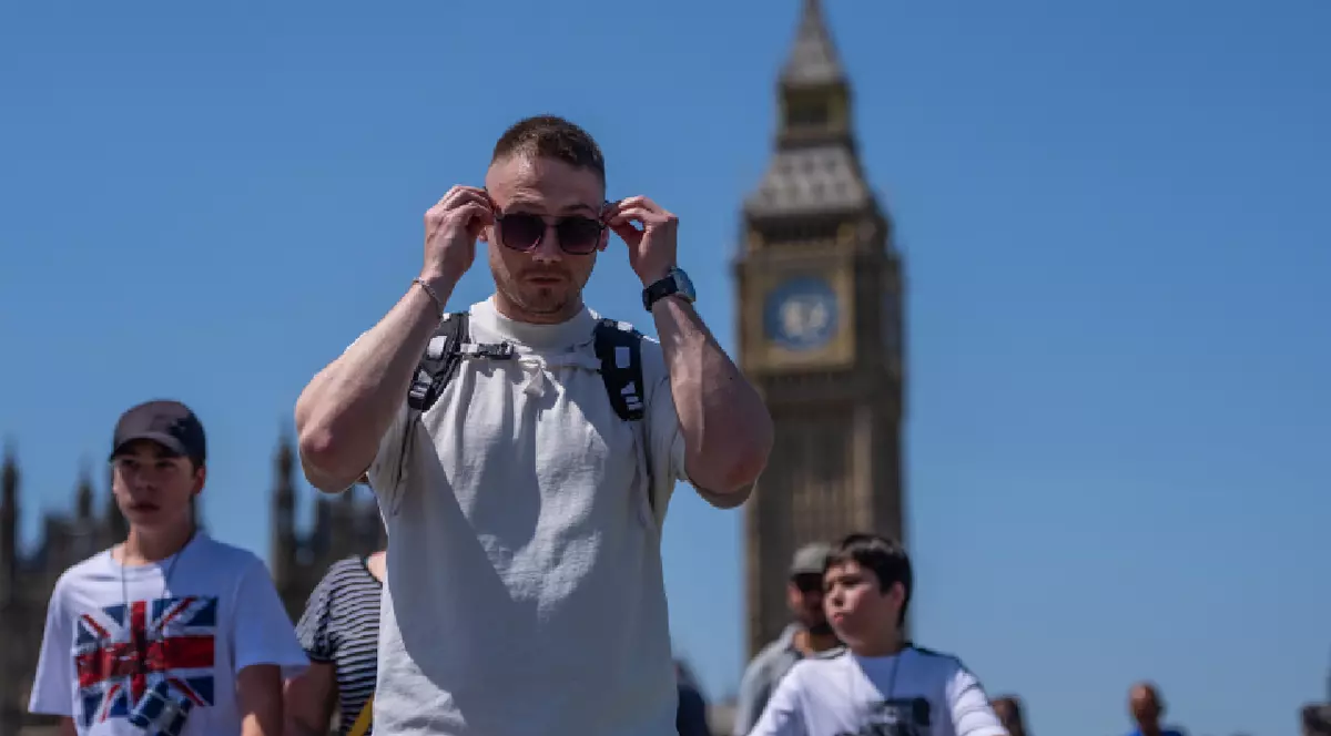 Un bărbat cu tricou alb își pune ochelarii de soare în timp ce se plimbă peste Podul Westminster cu familia sa pe 26 mai 2026 la Londra, Anglia.