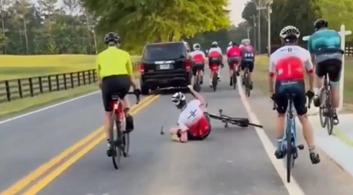 O mașină neagră care intră într-un grup de bicicliști. Unul dintre ei a căzut jos