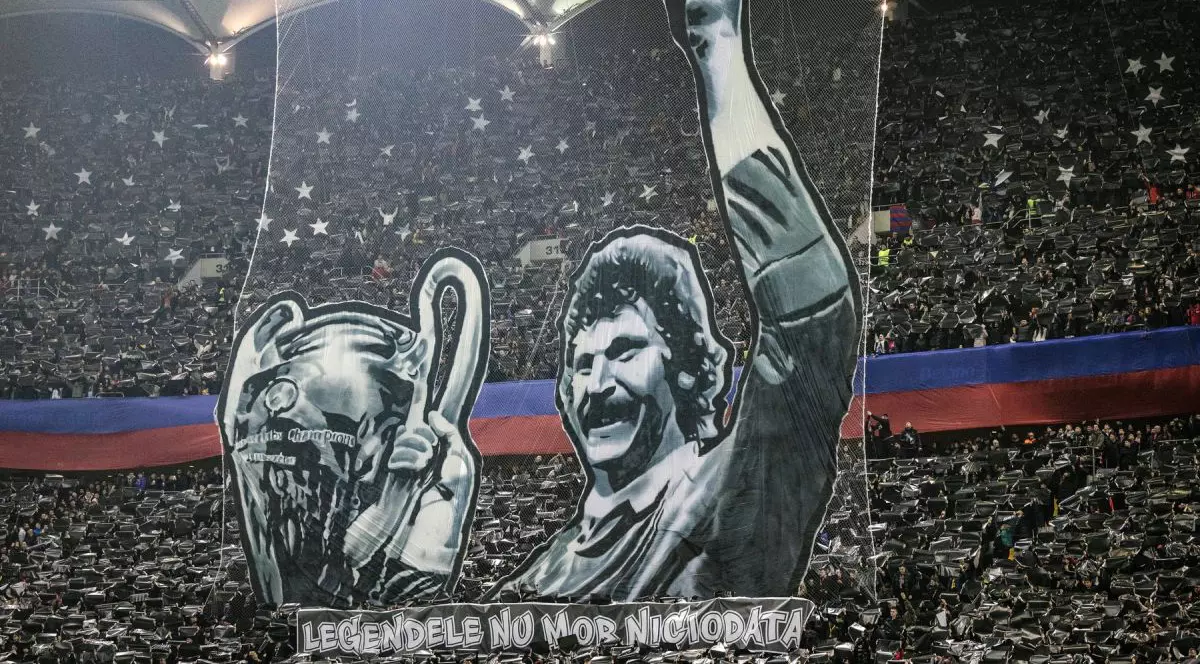 Suporteri pe un stadion de fotbal care au ridicat un banner cu Helmuth Duckadam și Cupa Campionilor Europeni câștigată de Steaua București în 1986