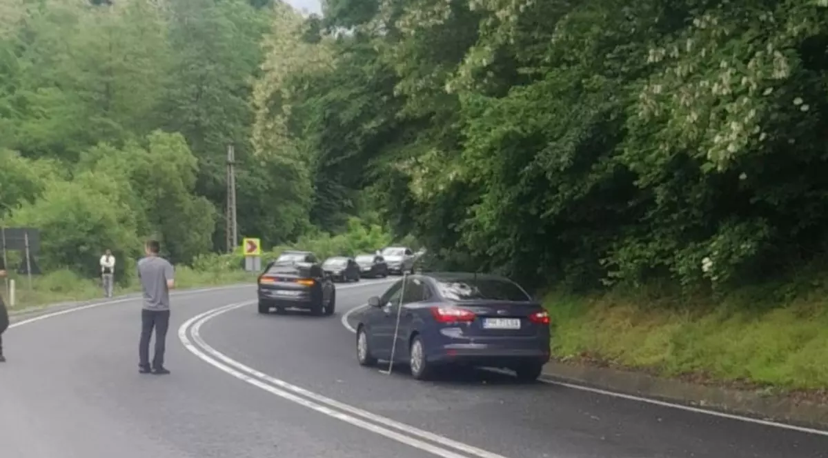 Mai multe mașini care au fost oprite în coloană, pe un singur sens de mers și care așteaptă să fie delocat traficul, după un accident rutier. Unul dintre șoferi a ieșit din autoturism și stă pe stradă
