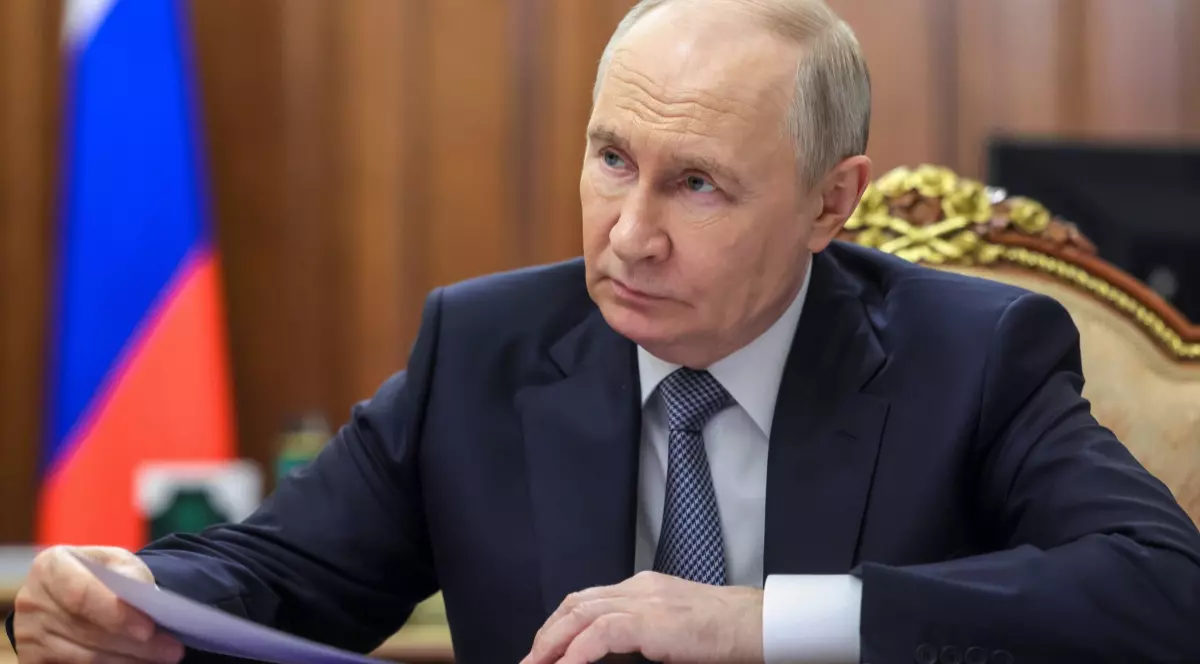 Vladimir Putin, într-un costum albastru, ăn biroul de la Kremlin, cu steagul Rusiei în spate