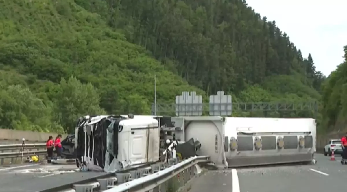 În imagine se vede un camion răsturnat pe o autostradă, după un accident grav care a blocat mai multe benzi de circulație. La fața locului intervin echipaje de urgență, în timp ce vehiculul avariat și resturile împrăștiate pe carosabil indică violența impactului.