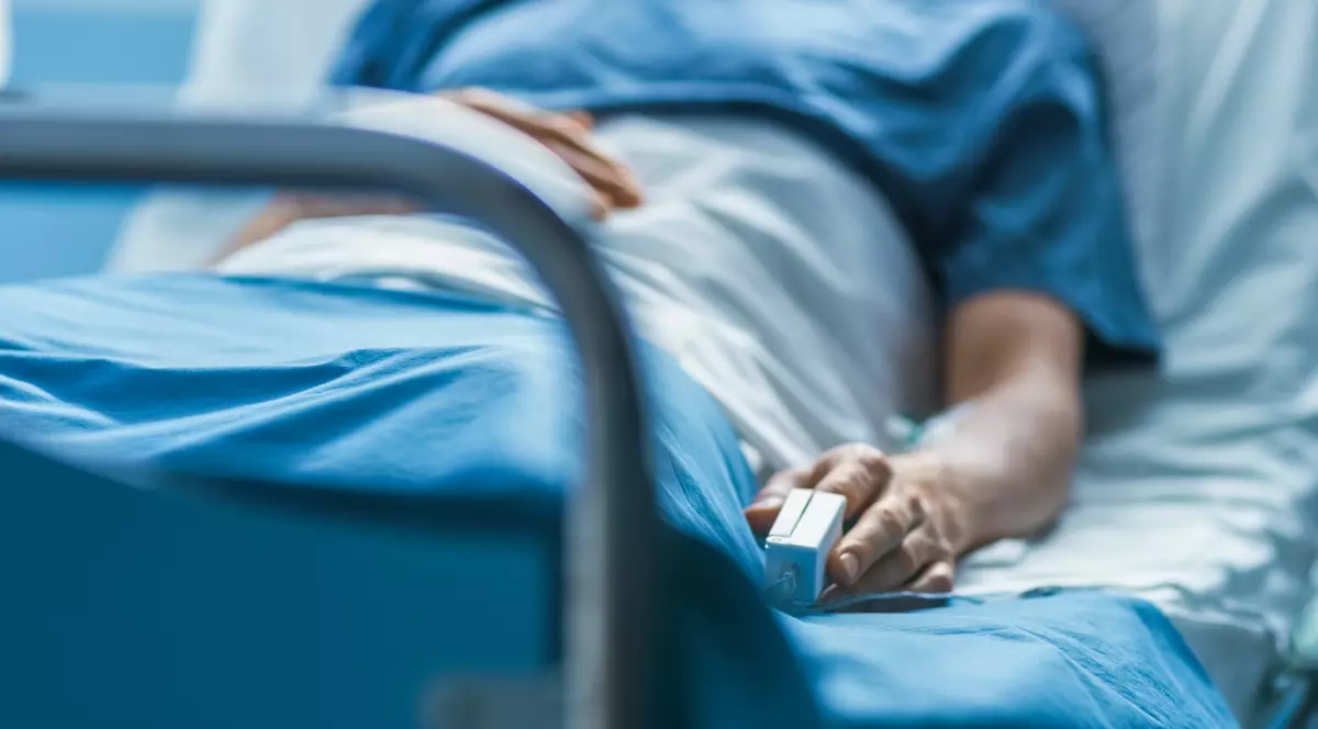 Un adolescent internat în spital, tânărul stă pe patul de spital cu o cămașă albastră pe el, are montat un monitor pentru oxigen și o branula