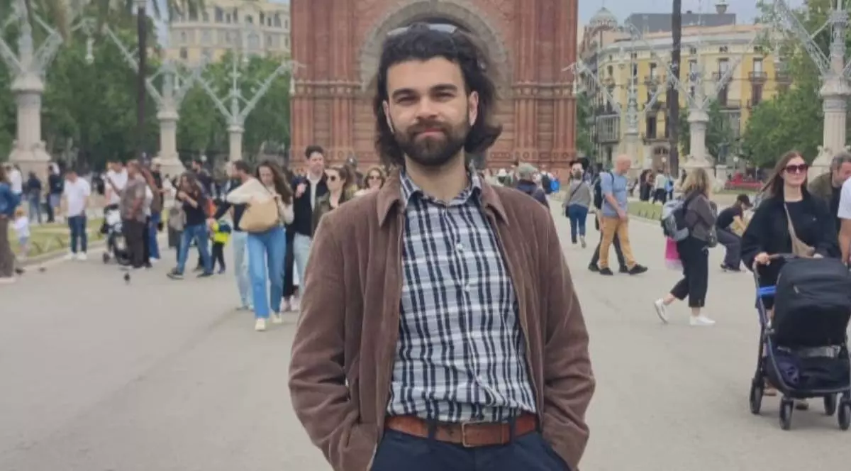 Andrei Mureșan, un inginer român din Spania, intr-o camasa in carouri cu all si negru, o camasa maro deschisa la nastruri, ochelari de soare pe cap, cu mainile in buzunar, pozeaza pe o strada cu multi oameni