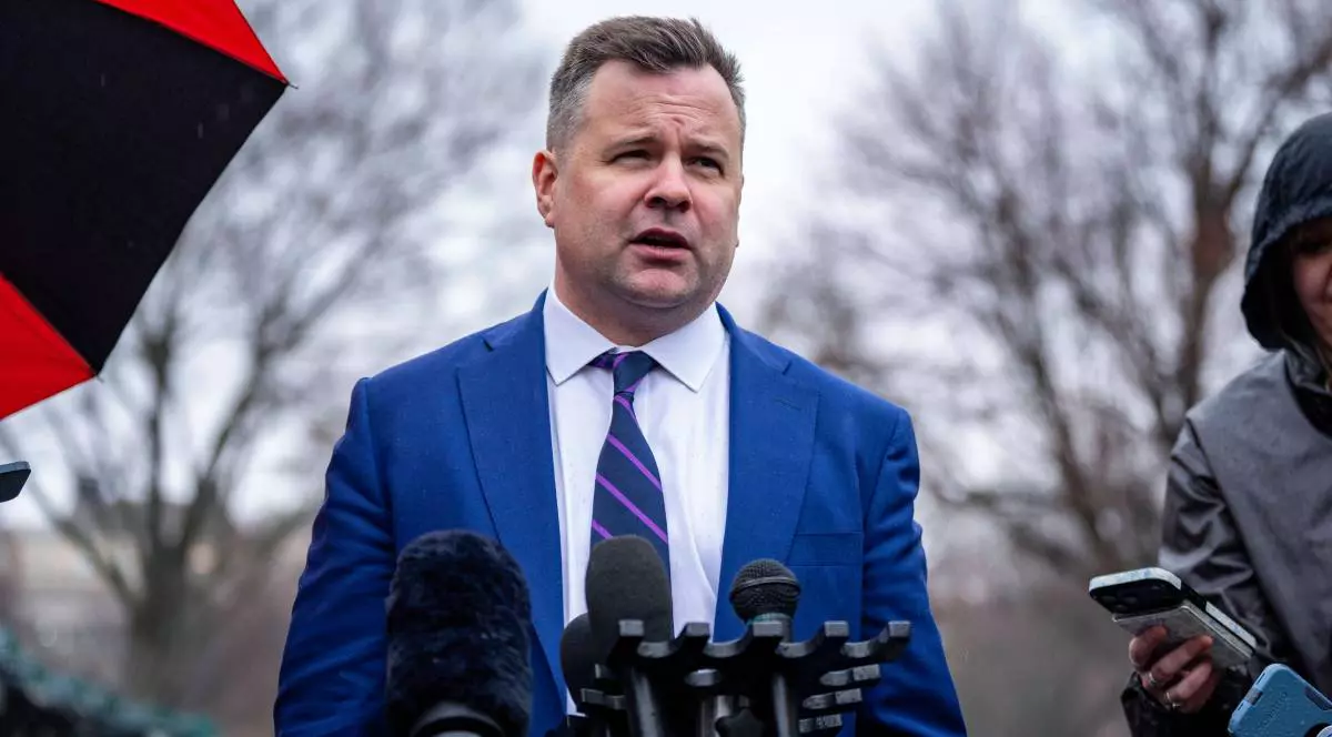 bill pulte, îmbrăcat într-o cămașă albă și un sacou albastru, afară, în timpul unei conferinte de presa, cu mai multe microfoane în fața lui.