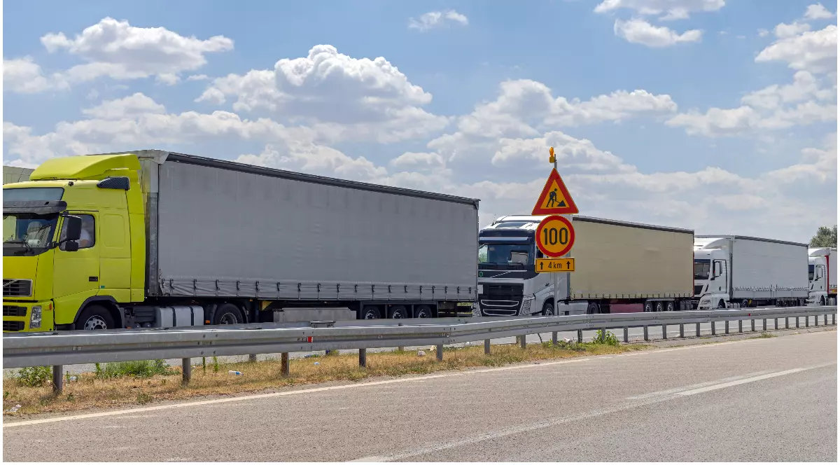 Mai multe camioane de diferite culori staționate în coloană, pe o autostradă