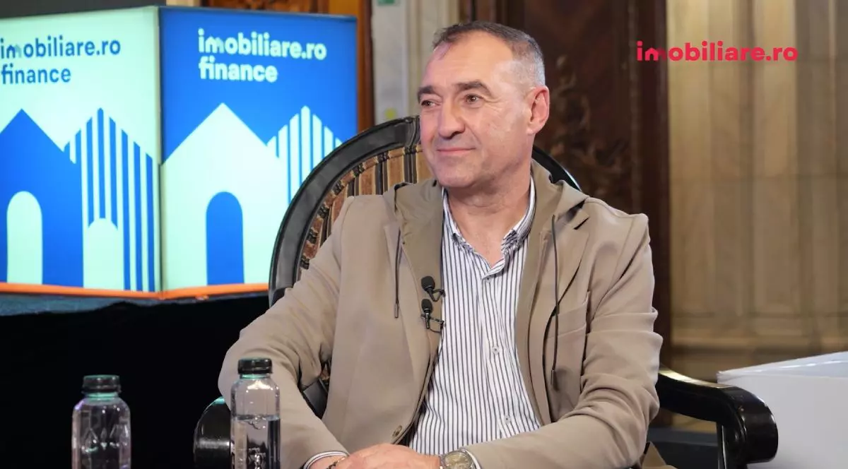 Cătălin Apetri, CEO al Horizon City, în timp ce stă pe fotoliu, îmbrăcat cu o cămașă albastră cu pătrățele și o geacă scurtă de culoare crem, iar pe fundal se vede logo-ul Imobiliare.ro