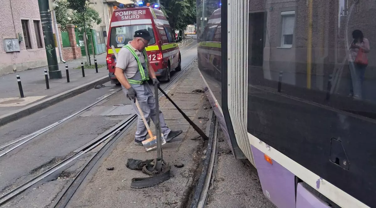 Un bărbat care încearcă să curețe șinele de tramvai cfu o mătură, în timp ce tramvaiul așteaptă să pornească, după ce afost blocat