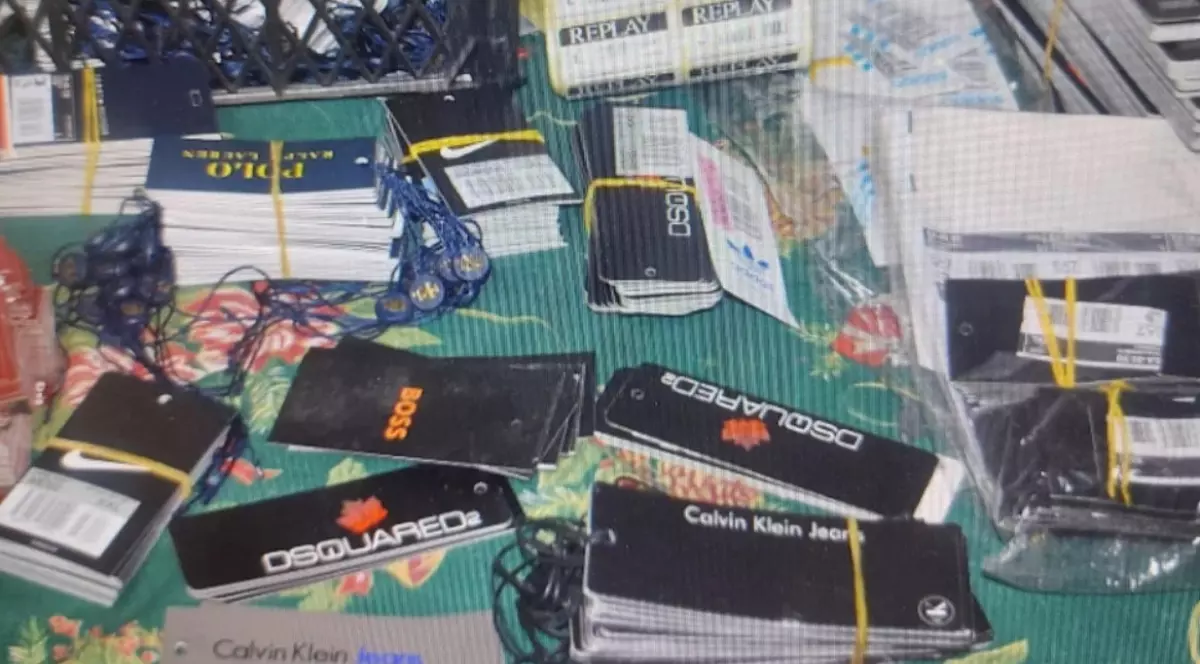 Teancuri de etichete din carton folosite pentru îmbrăcăminte, purtând logo-uri ale unor mărci cunoscute precum Polo Ralph Lauren, Nike, Boss, Dsquared2 și Calvin Klein Jeans, așezate pe o masă.