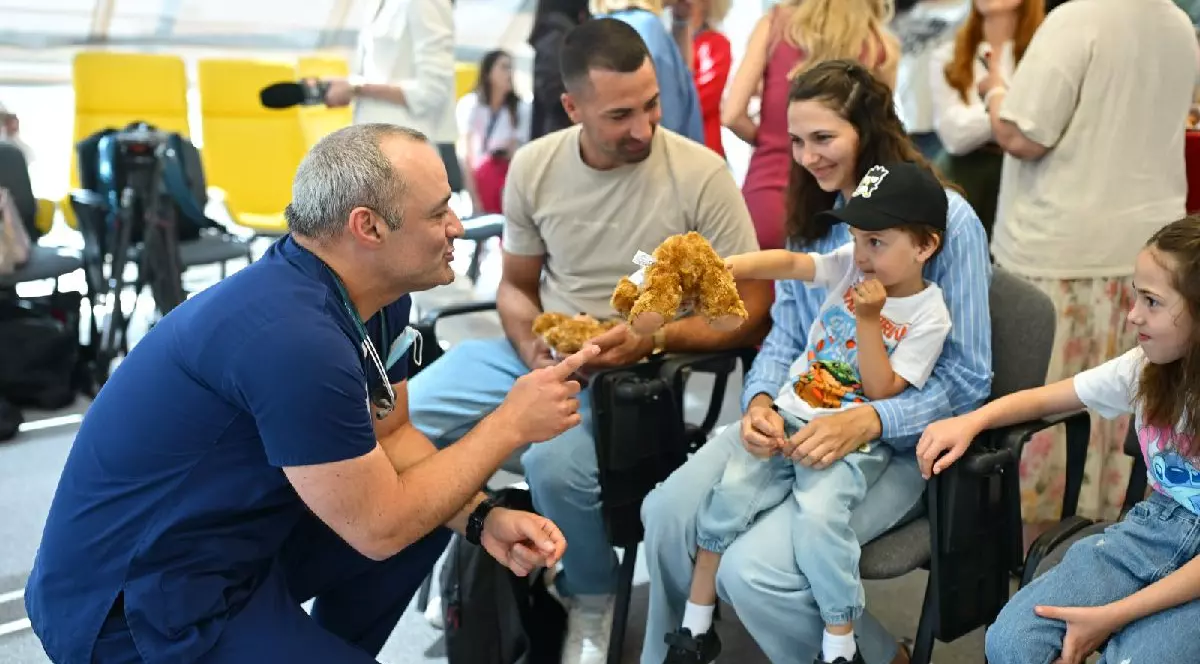 Un medic tine un ursulet de plus in mana si vorbeste cu un baietel si parintii lui. Medic cardiolog, copii operati pe inima