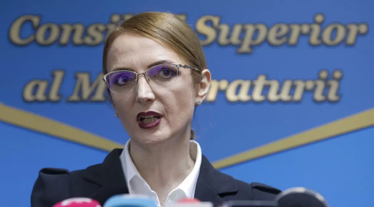 Lia Savonea îmbrăcată într-un sacou negru cu cămașă albă vorbește la microfon c. În spatele ei scrie Consiliu Superior al Magistraturii.