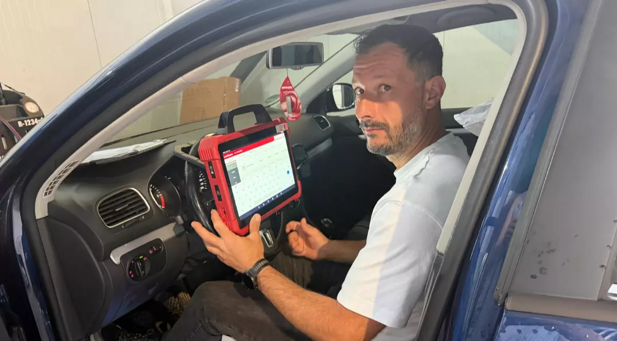 Mihai Avram, un bărbat înalt cu pantaloni negrii și tricou alb, în timp ce stă la volanul unei mașini