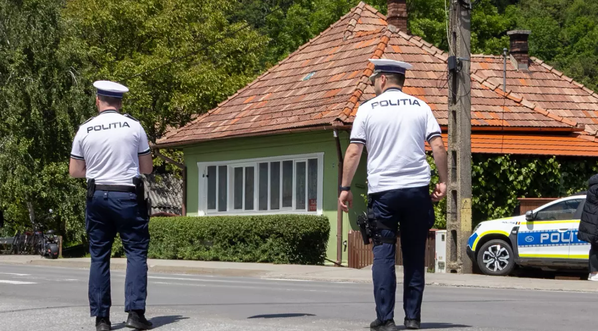 Doi polițiști care merg pe stradă, în fața lor este parcată mașina de Poliție