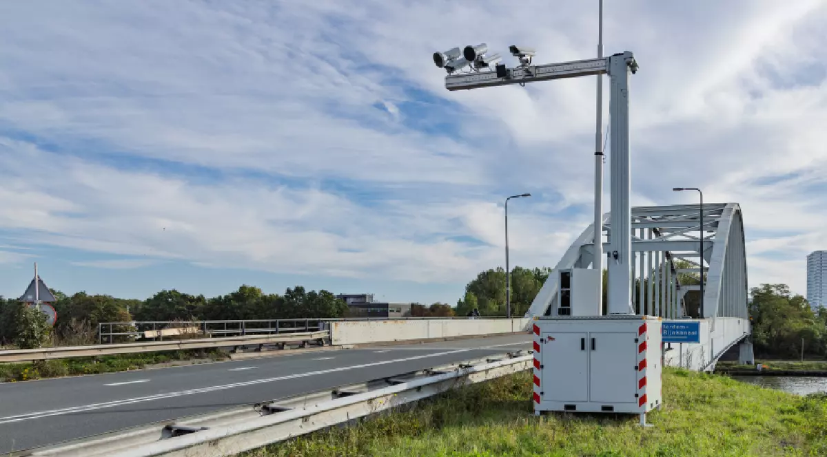 O unitate de camere mobile pentru monitorizarea traficului, utilizarea telefonului și aplicarea legii, poziționată pe un mal înverzit lângă un pod rutier și arcuit, în Țările de Jos.