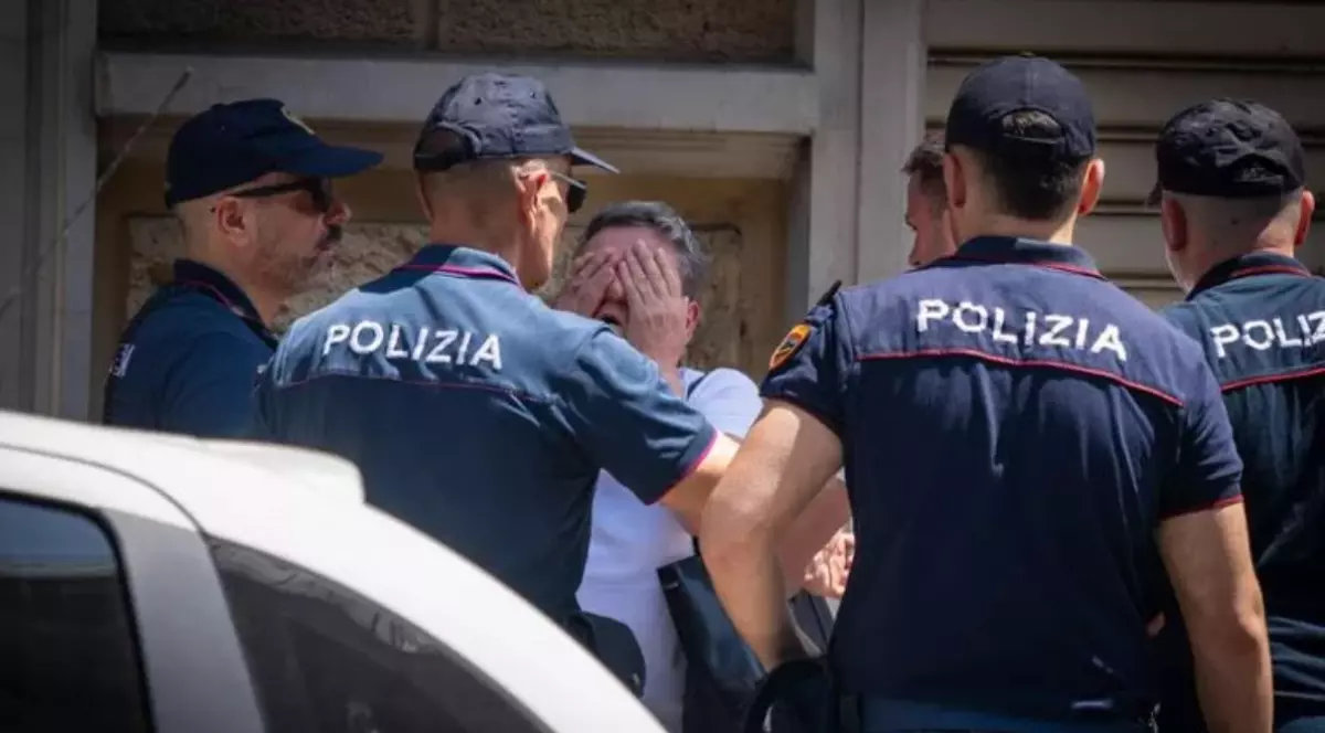 Un grup de polițiști italieni în uniforme, adunați în jurul unei persoane care își acoperă fața cu ambele mâini într-un gest de disperare sau suferință.