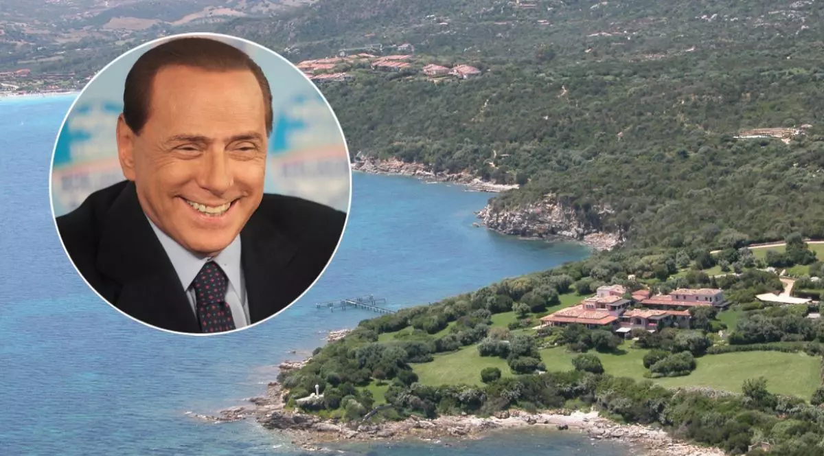Imagine aeriană cu Villa Certosa din Sardinia și Marea Mediterană, iar într-o oglindă apare Silvio Berlusconi, îmbrăcat cu costum negru, cămașă și cravată, în timp ce zâmbește
