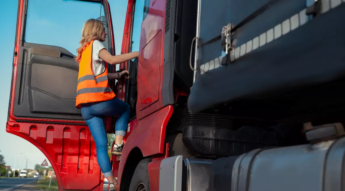 Imaginea arată o tânără cu vestă portocalie urcând în cabina unui camion roșu