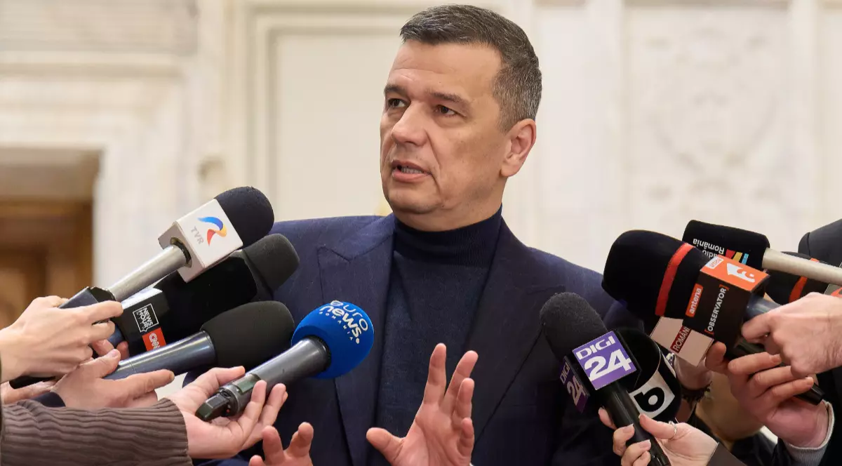 Sorin Grindeanu îmbrăcat în sacou bleumarin și maletă închisă la culoare, vorbind și gesticulând în fața jurnaliștilor.