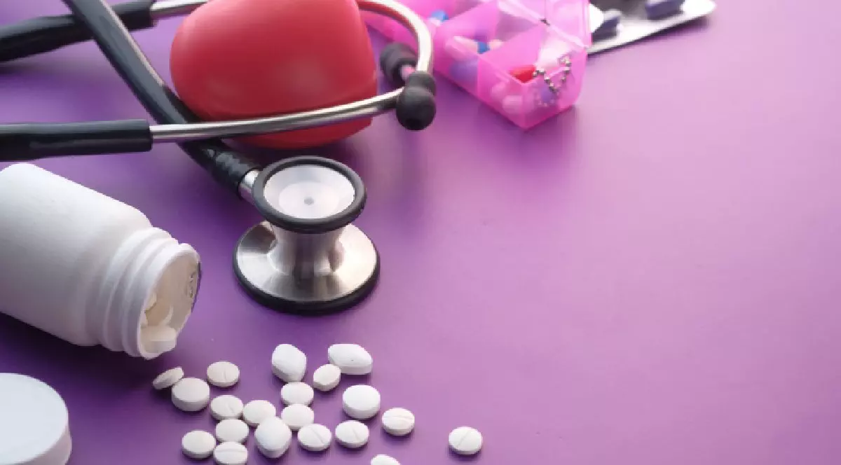 O inima si un stetoscop pe o masa mov si un flacon rasturnat cu medicamente . Bolnavi de inima