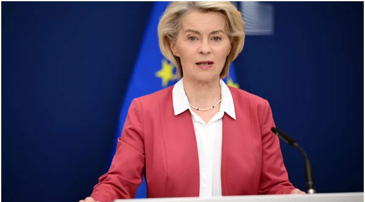 Ursula von der Leyen, îmbrăcată într-un sacou roșu și cămașă albă, în timpul unui discurs, având în spate steagul european