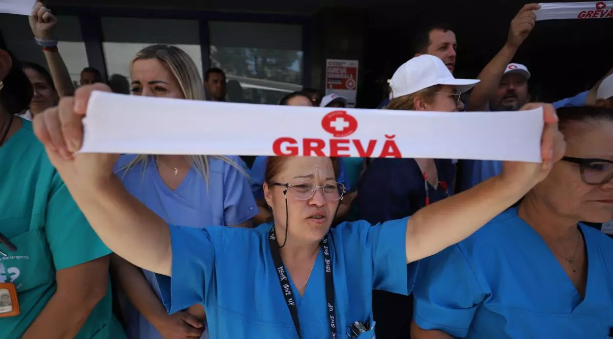 Asistentă medicală îmbrăcată în uniformă albastră, lângă alți colegi, cu o bandană albă pe care scrie grevă cu roșu, pe 29 iulie 2026, la greva din spitale