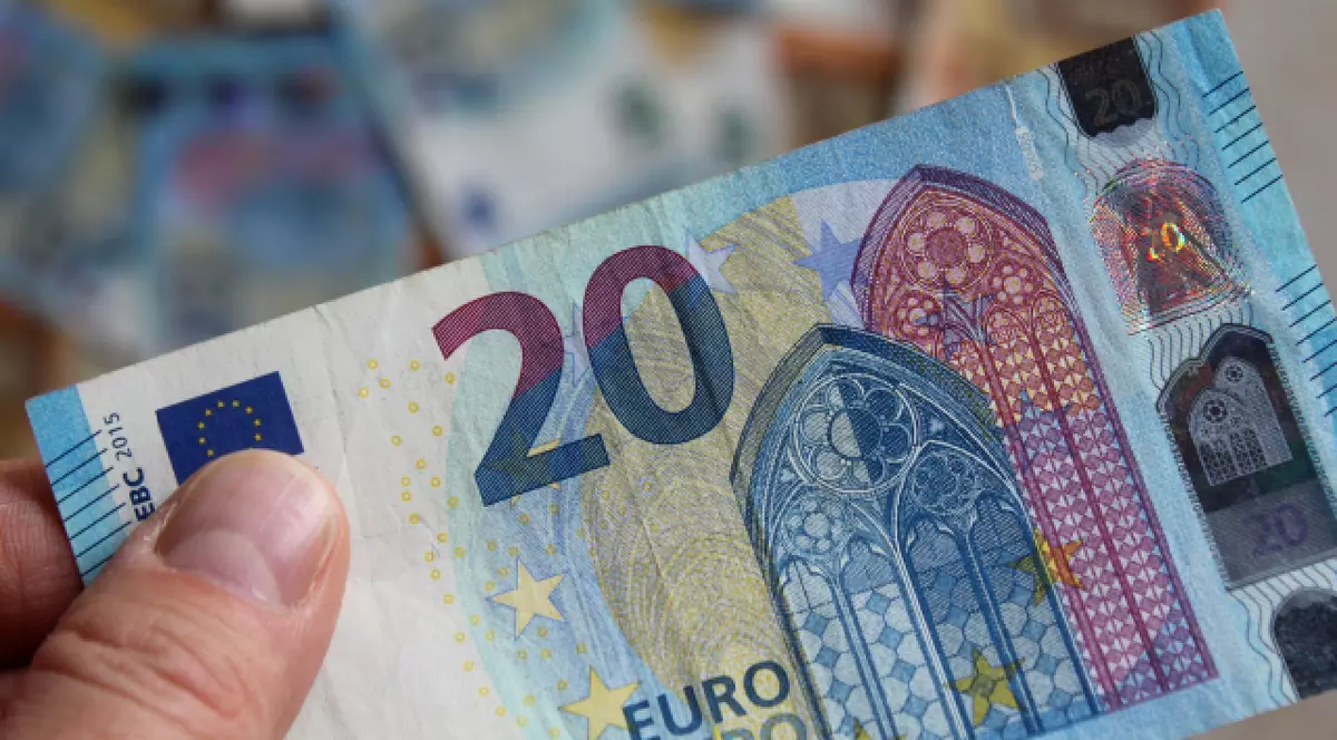 Un bărbat șine în mână o bancnotă de 20 de euro