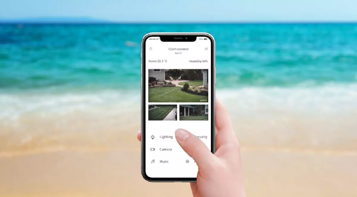 Cum îţi laşi casa în siguranţă înainte de a pleca în concediu - Aplicația „Cam control” pe ecranul unui telefon, ținut în mână pe o plajă. Foto: Shutterstock.com