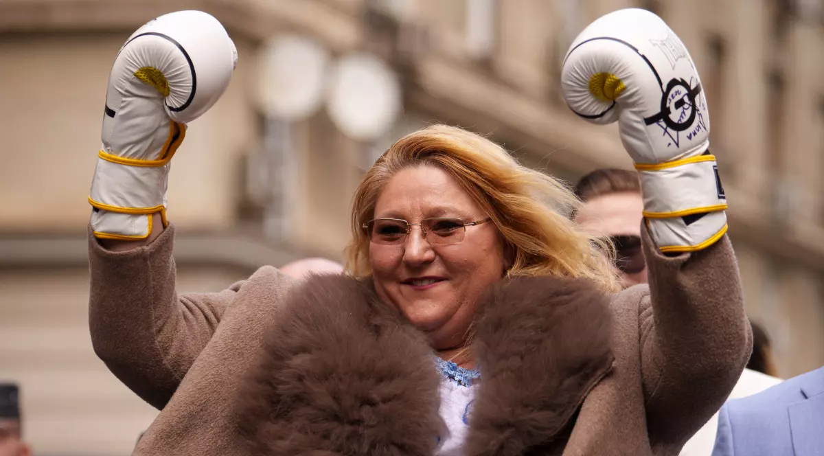 Imaginea o surprinde pe Diana Șoșoacă purtând mănuși de box și ridicând brațele în aer, în timpul unui eveniment desfășurat în aer liber.