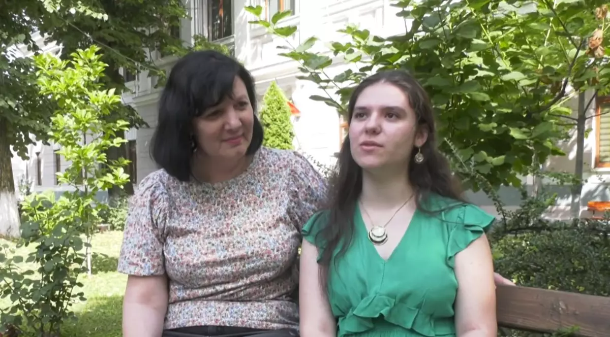 Ana Maria, singura elevă din Olt care a avut media 10 la BAC, cu o rochie verde, în timp ce stă pe bancă alături de profesoara ei