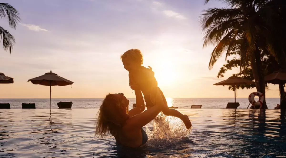 Ghidul siguranței la piscină sau la mare - O mamă își ridică fiul în brațe, în timp ce se află în piscină, la apus