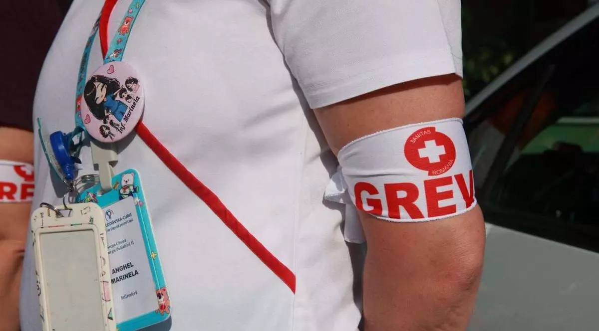 O mână a unei asistente pe care este înfăsurată o banderolă ăe scare scrie: grevă