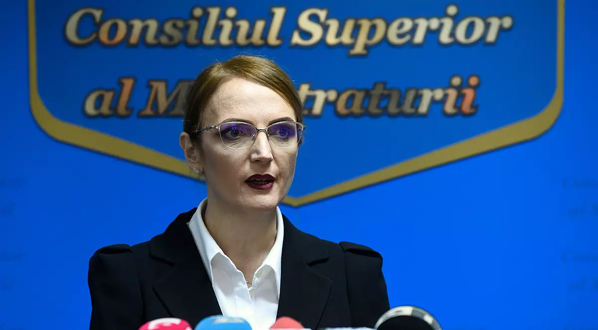 Lia Savonea îmbrăcată într-un sacou negru cu cămașă albă vorbește la microfon c. În spatele ei scrie Consiliu Superior al Magistraturii.