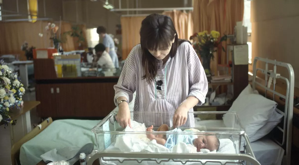 O mama stă în picioare lângă copilul ei nou născut, într-un salon de spital