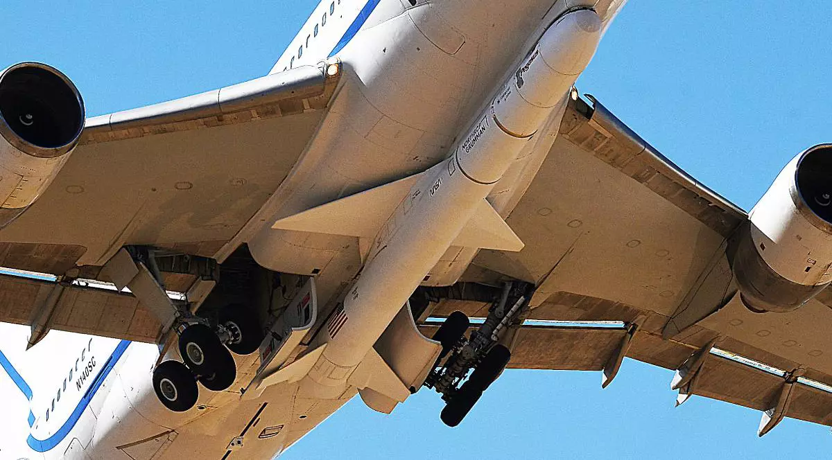 Un avion alb transportă o rachetă prinsă de partea dorsală a fuzelajului său.