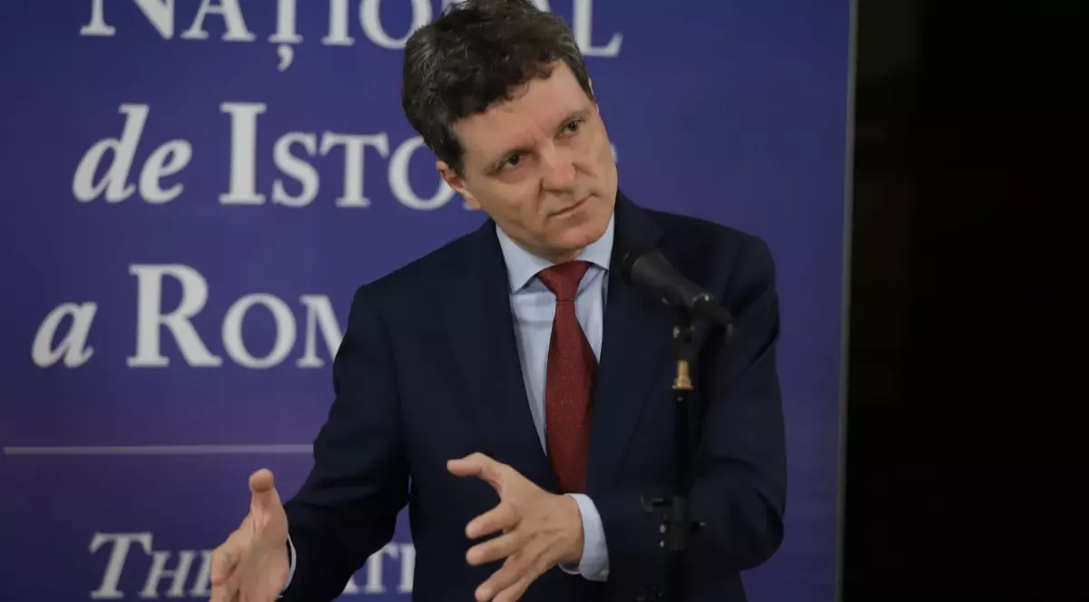 Președintele Nicușor Dan, îmbrăcat la costum și purtând o cravată roșie, gesticulează în timpul unei conferințe de presă susținută la Muzeul de Istorie