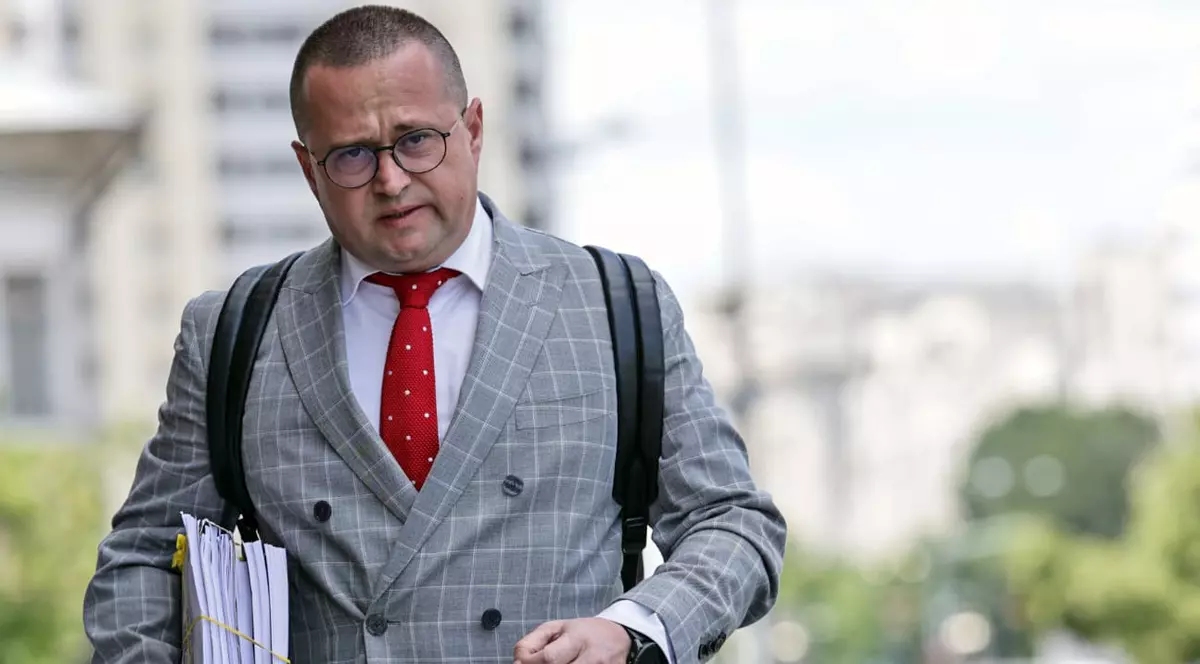 Un avocat imbracat în costum gri su cravata rosie intra cu un dosar in mana in tribunal