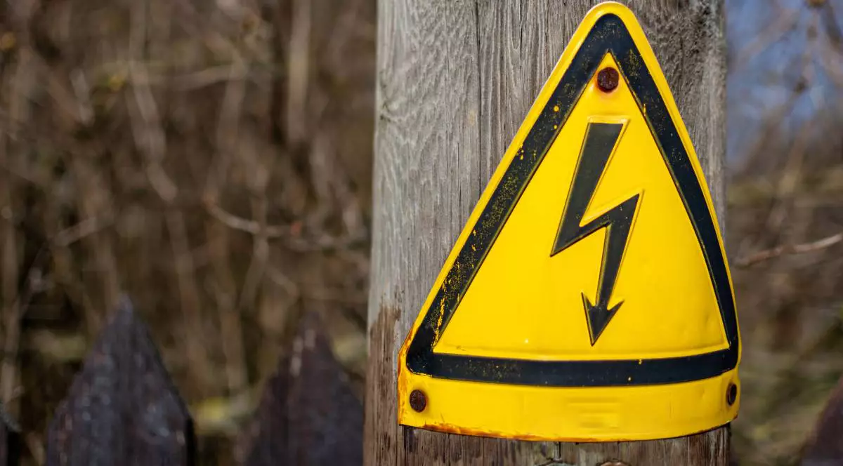 Semn la baza unui stâlp electric din lemn care avertizează asupra pericolului de electrocutare în cazul în care se încearcă urcarea pe stâlp lângă o stradă.