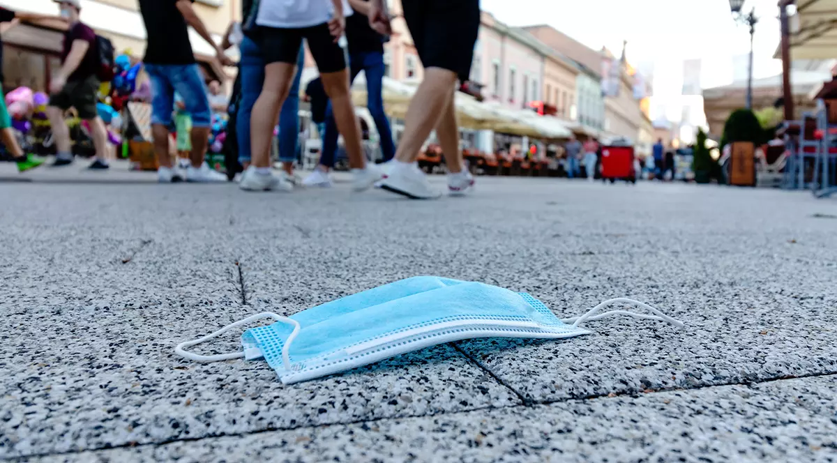 Improperly discarded medical face mask thrown away after use on the street footpath. COVID-19 waste or litter concept