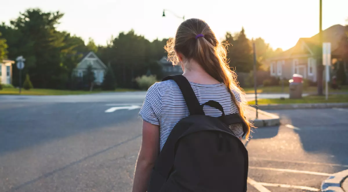 Profilul unei adolescente deprimate/triste la apusul soarelui, într-o parcare, purtând un rucsac.