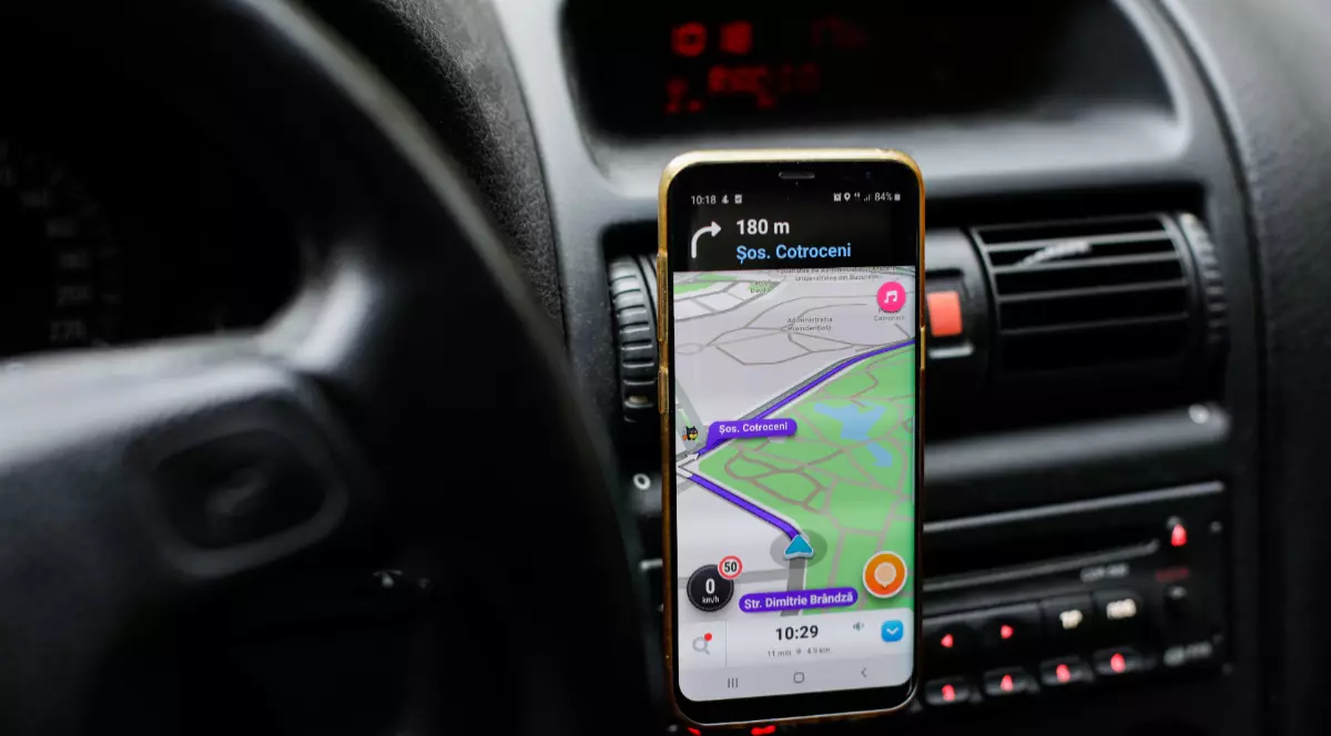 Imaginea prezintă un smartphone montat pe bordul unui automobil, rulând aplicația de navigație Waze ce afișează un traseu pe Șoseaua Cotroceni.