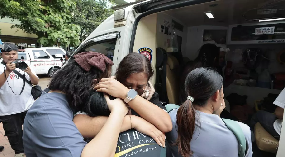 Prietenii unui profesor rănit, care a fost transportat în ambulanță, se îmbrățișează la locul atacului armat dintr-o școală, în provincia Nonthaburi din Thailanda.