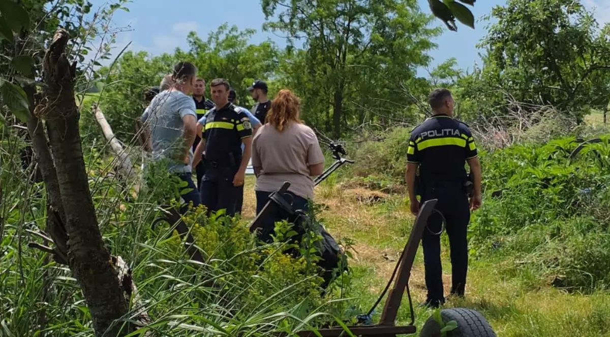 Imaginea prezintă un grup de polițiști români și civili adunați într-o zonă rurală cu verdeață și vegetație deasă în cadrul unei anchete.