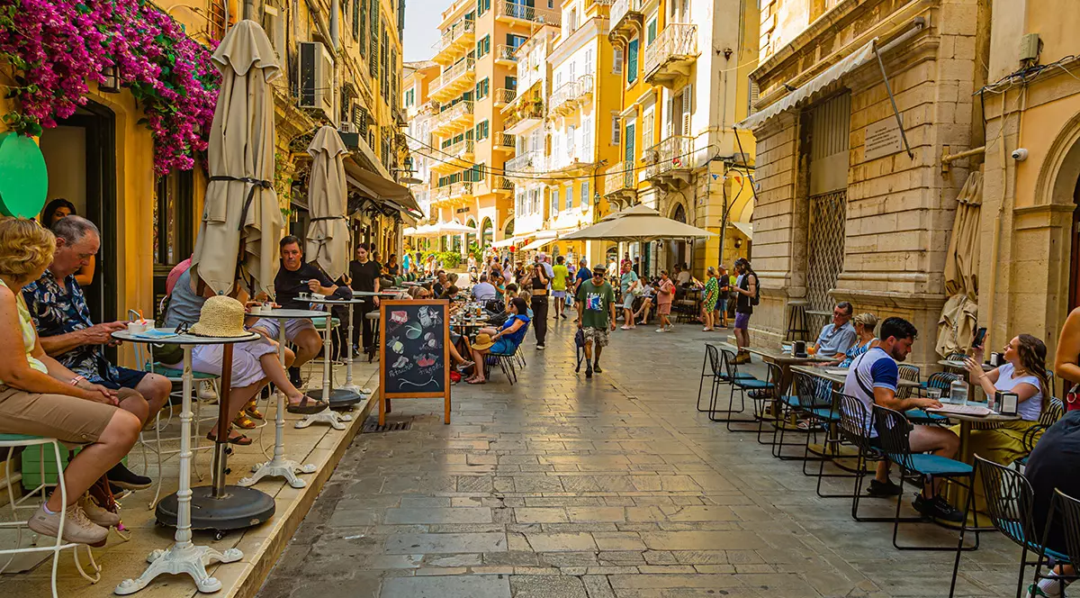O stradă din Corfu cu rerstaurante și mulți clienți la mese.