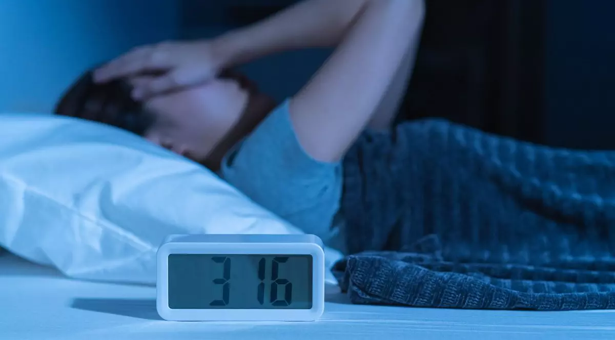 Tânără asiatică iritată, stresată, anxioasă, care suferă de insomnie, frustrată că stă trează în pat noaptea, cu dureri de cap sau migrene, cu probleme de sănătate, deranjată de zgomotul puternic, incapabilă să adoarmă.