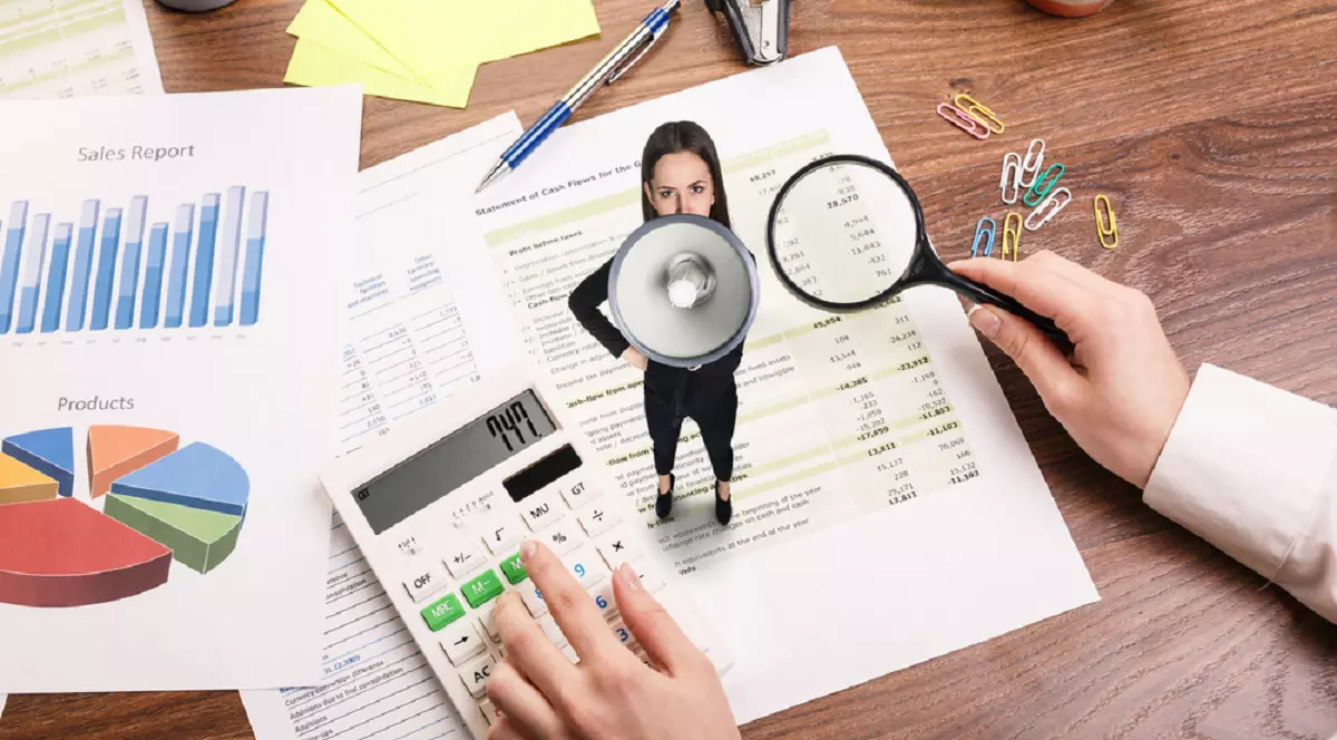 Ce este loud budgeting, tendința financiară populară la generația Z - Imagine cu o femeie, în miniatură, cu portavoce aşezată pe o factură, lâgă un calculator de birou