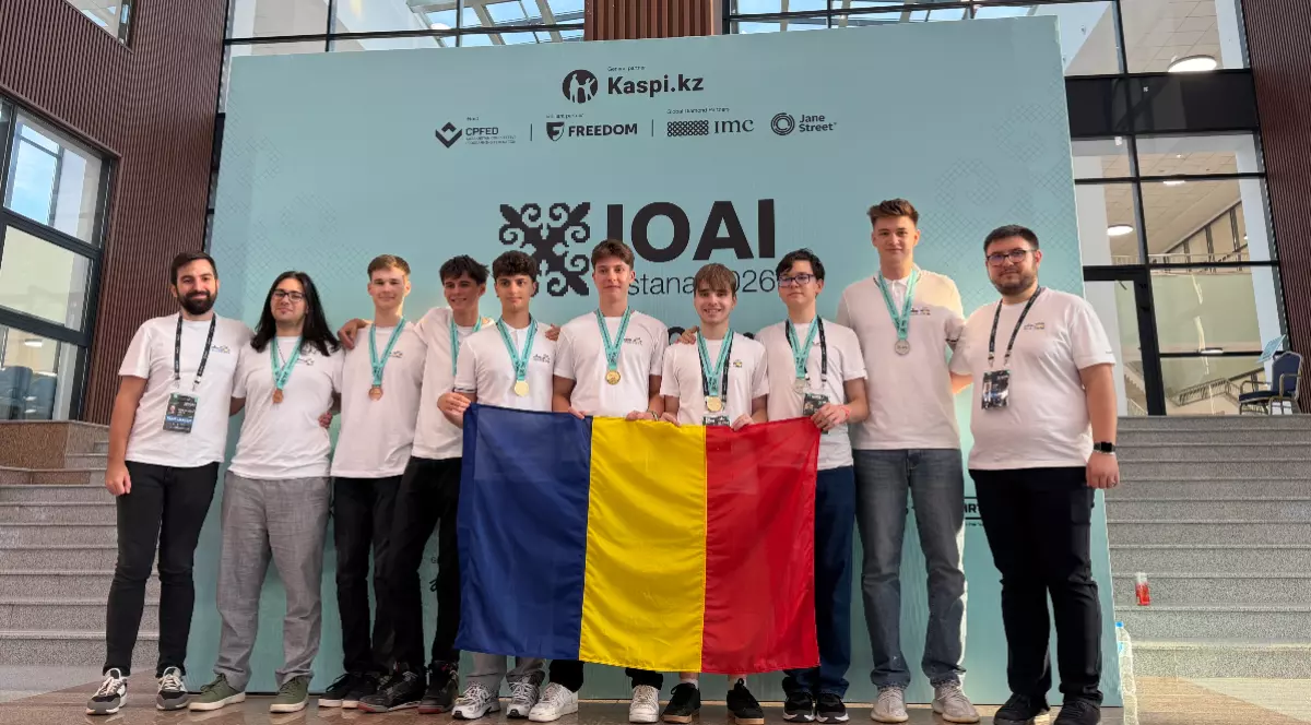 În imagine este surprins lotul României la Olimpiada Internațională de Inteligență Artificială (IOAI), alături de coordonatori, după obținerea medaliilor, având în față drapelul României. Fotografia ilustrează performanța elevilor români în competiția internațională și succesul echipei la ediția din 2026.
