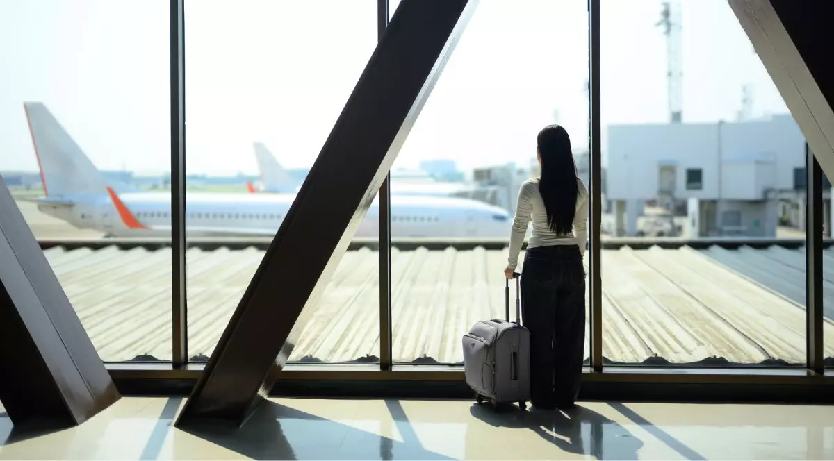 O tânără din Generația Z, aflată în călătorie, așteaptă cu valiza în mână, privind avionul de la fereastra aeroportului.