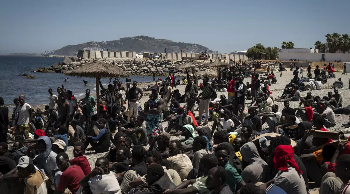 Migranți așteaptă pe plajă, lângă centrul CETI (Centrul de Ședere Temporară pentru Imigranți), la 2 august 2026, în Ceuta, Spania